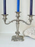 Vintage silver coloured three-arm candelabra with ornate base and soft patina, photographed on a white surface