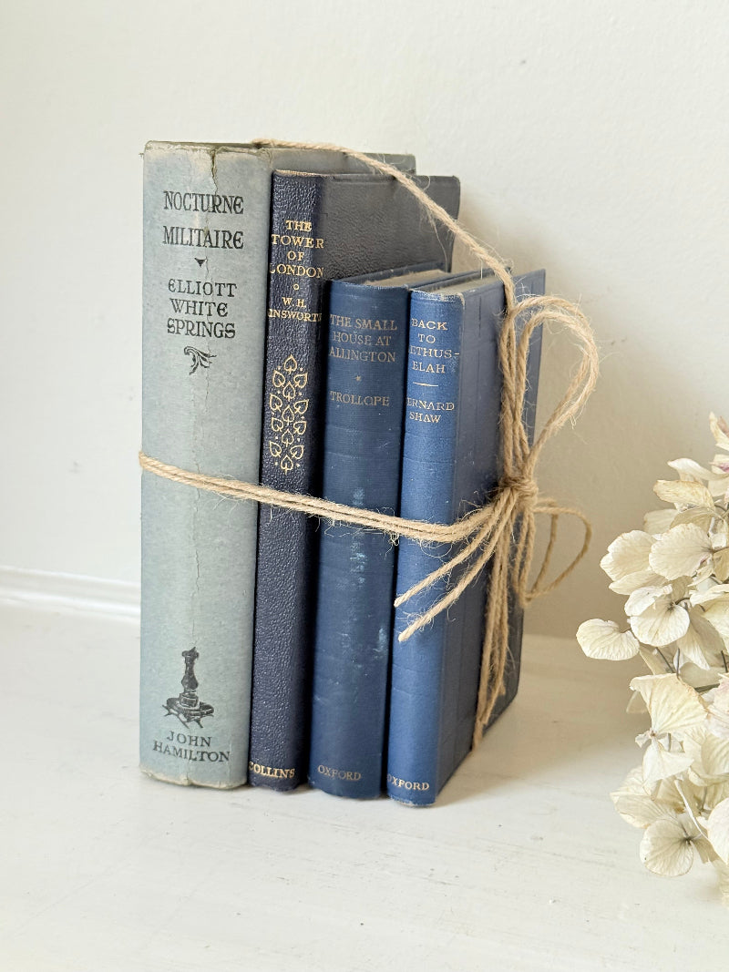 Vintage decorative book bundle in navy, grey, and cream tied with twine, photographed on a white surface