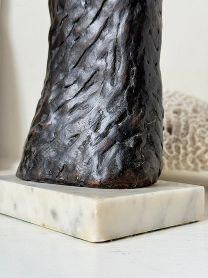 Solid bronze figure of a standing semi nude woman with upswept hair on a white marble base