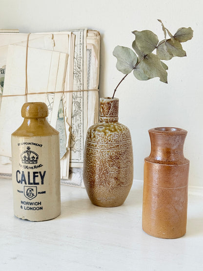 Three antique stoneware bottles, a printed Caley of Norwich and a Portuguese Campos Filhos, photographed on a white surface