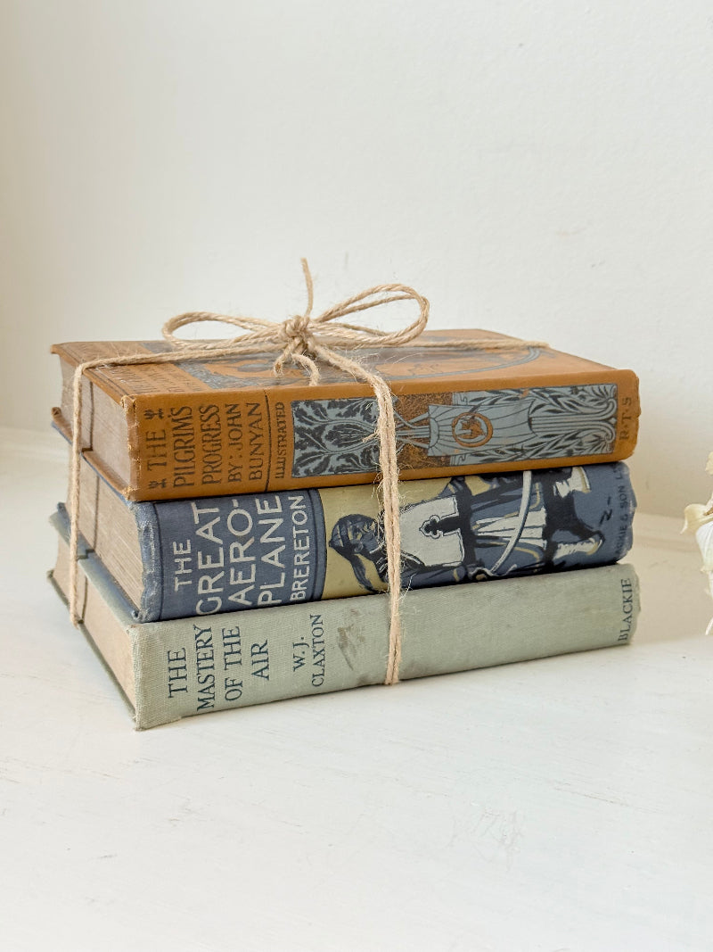 Vintage decorative book bundle in blue, grey, and ochre tied with twine, photographed on a white surface