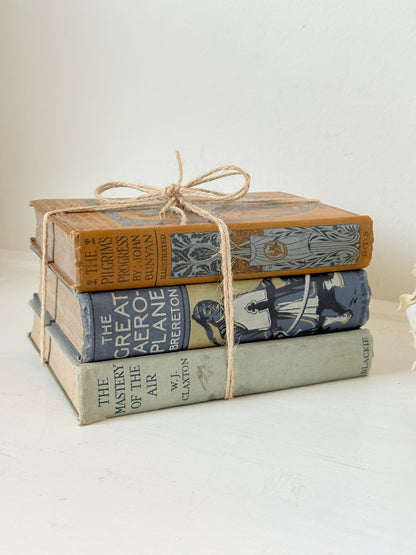 Vintage decorative book bundle in blue, grey, and ochre tied with twine, photographed on a white surface