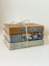Vintage decorative book bundle in blue, grey, and ochre tied with twine, photographed on a white surface