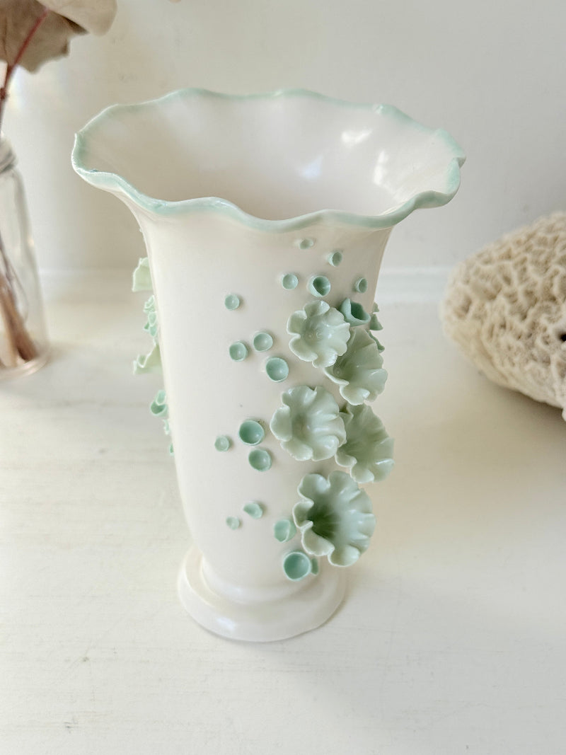 White Chessell Pottery studio vase with rippled rim and raised aqua floral decoration photographed on a white surface
