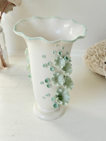 White Chessell Pottery studio vase with rippled rim and raised aqua floral decoration photographed on a white surface