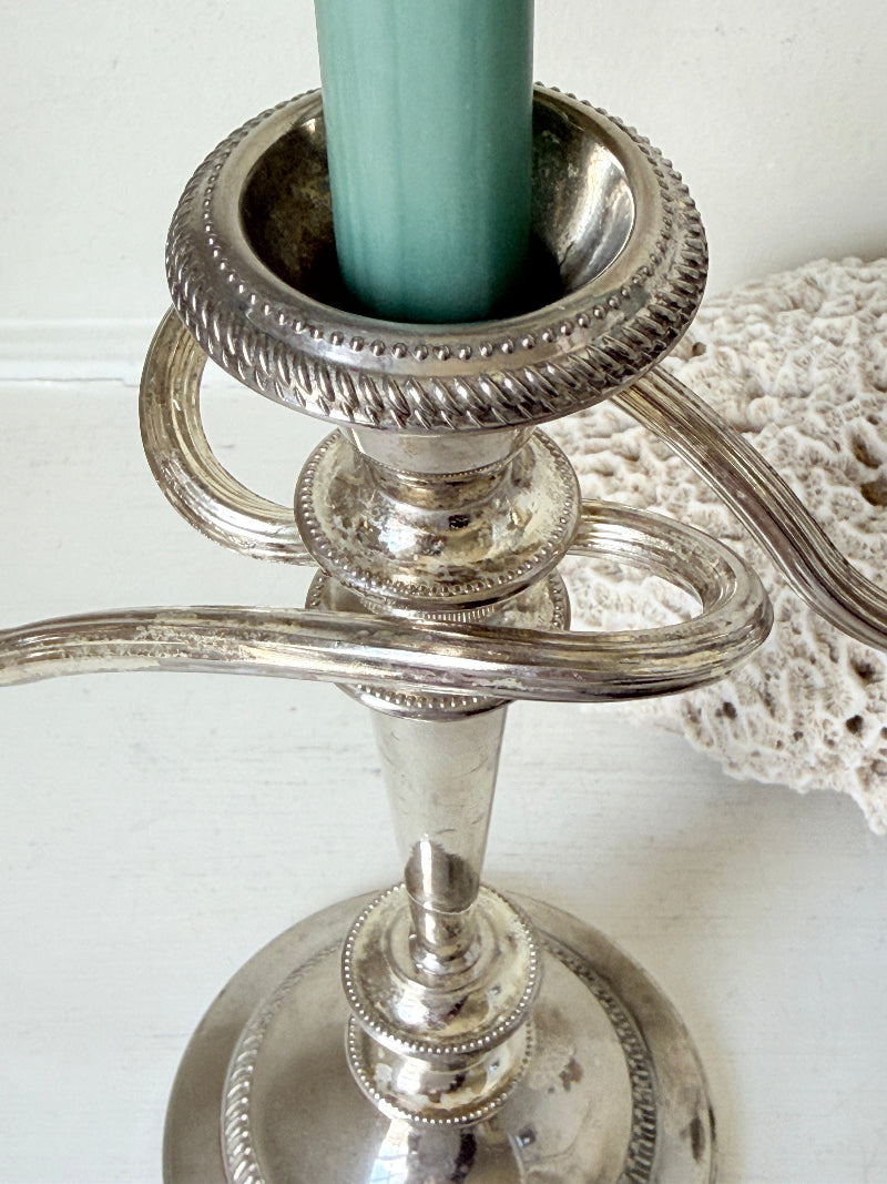 Vintage silver plated three arm candelabra with gadrooned detail and blue green taper candles styled on a white surface