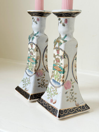 Pair of porcelain candle holders with hand-painted floral and vase motif in muted greens, pinks, and gold, styled with blush pink taper candles.