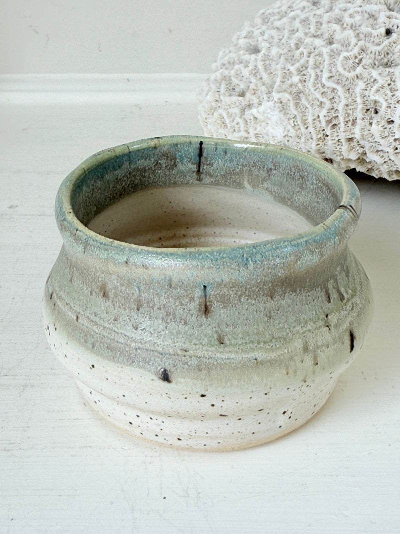 Studio pottery olive pot with soft green and cream glaze, photographed on a white surface