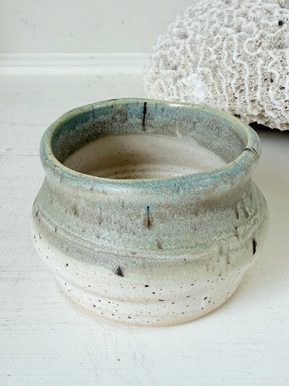 Studio pottery olive pot with soft green and cream glaze, photographed on a white surface