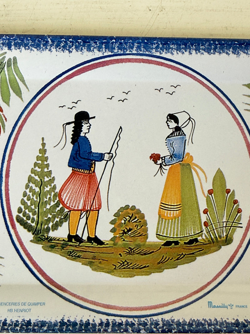 A square ceramic tile featuring a traditional French illustration of a man and woman in historical clothing, set within a circular frame with a blue and red border on an off-white background.