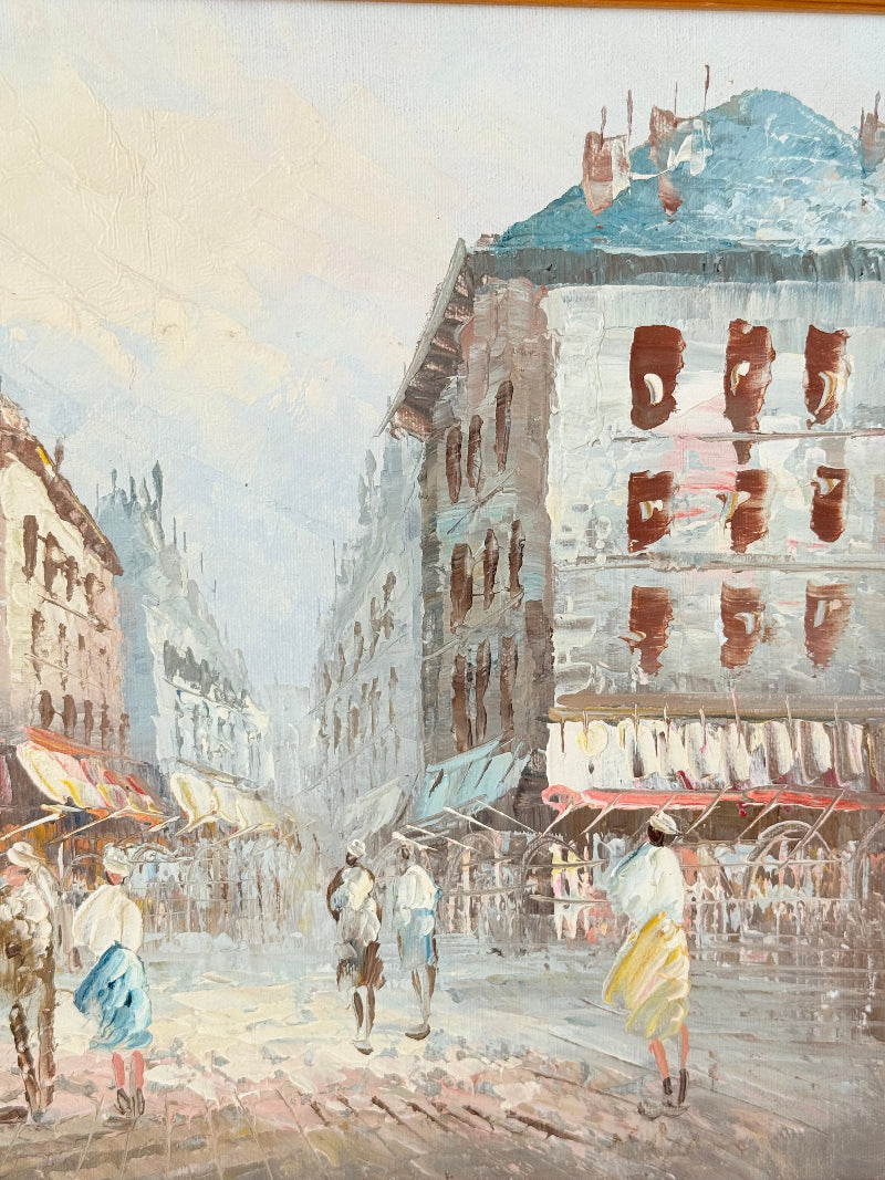 Vintage oil painting of European street scene with buildings and awnings in wooden frame photographed on a white surface

