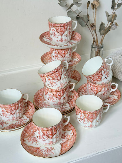 Vintage coral transferware coffee cans and saucers with scalloped edges and gold accents, set of ten, styled on a white surface.