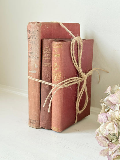 Bundle of three vintage books in worn rose and blush tones tied with natural twine, photographed on a white surface