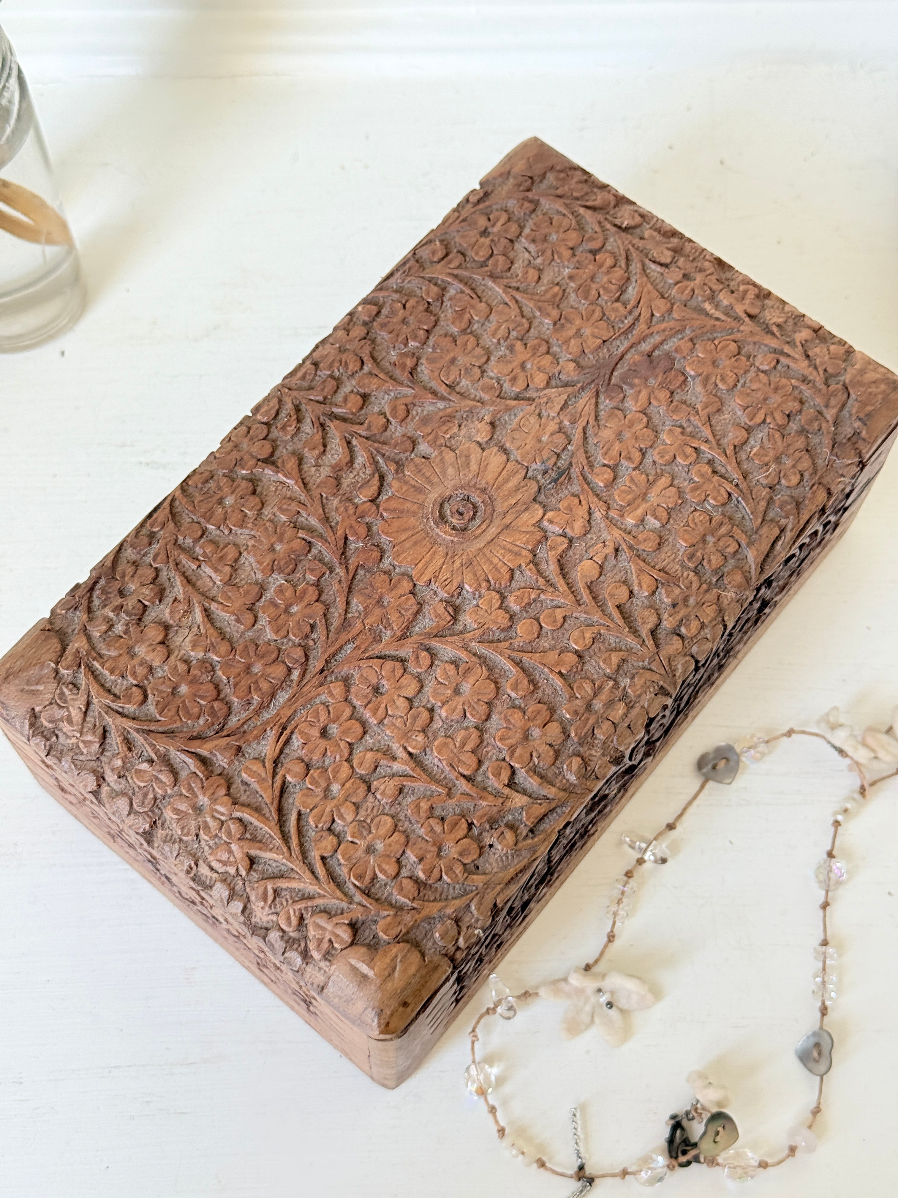 Vintage floral carved wooden jewellery box with detailed hand carved decoration, photographed on a white surface