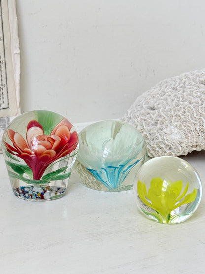 Trio of vintage glass paperweights with red flower, yellow flower and turquoise swirl decoration in clear coloured glass
