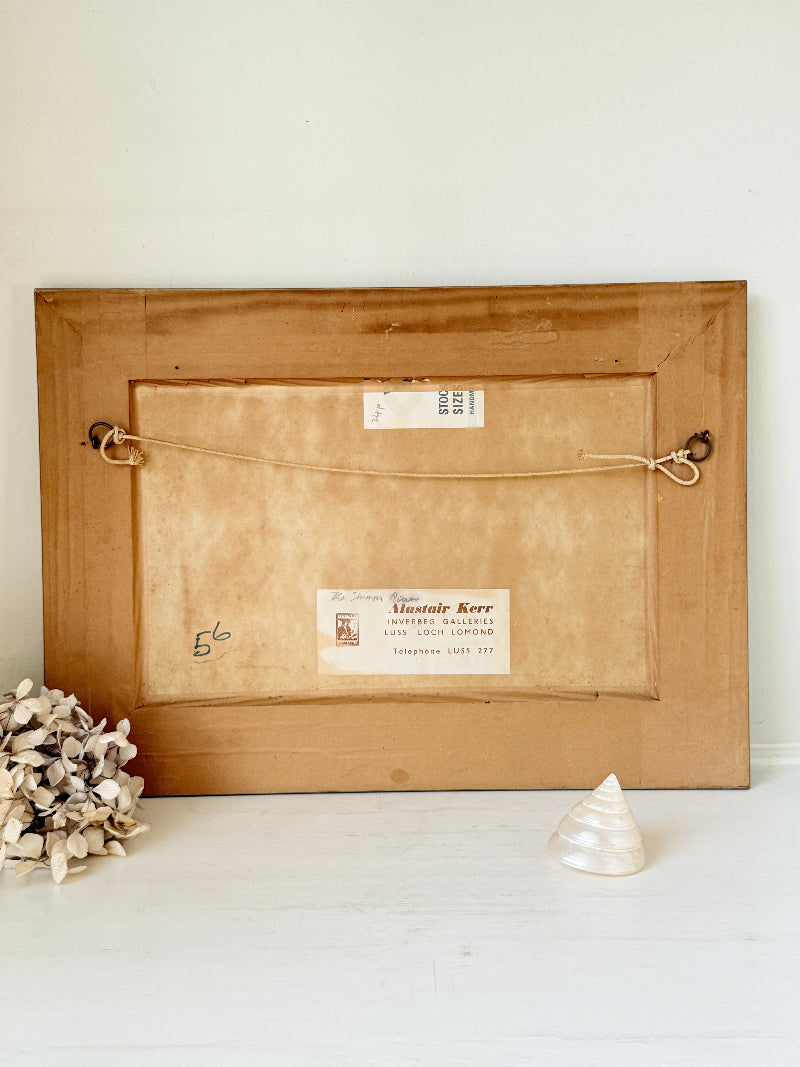 The back of a vintage wooden picture frame leaning against a white wall, with a hanging cord, mounting holes, and a paper label that reads &