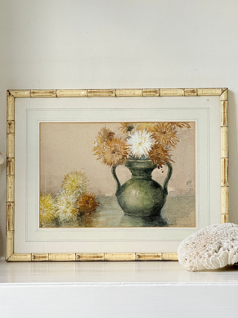 Vintage watercolour of chrysanthemums in green vase, under glass, in cream faux bamboo frame, photographed on white surface.