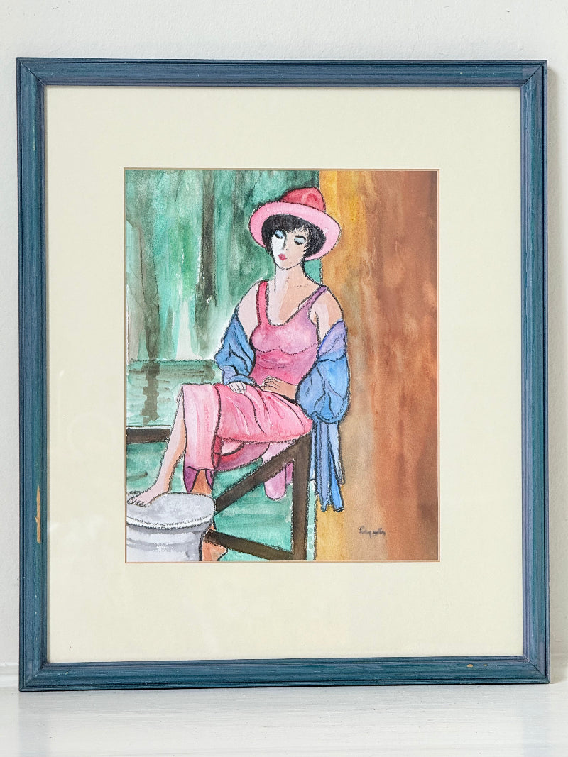 Vintage bright watercolour portrait of a seated woman in pink hat and dress with blue jacket, framed in blue wood with off-white mount, photographed on a white surface.
