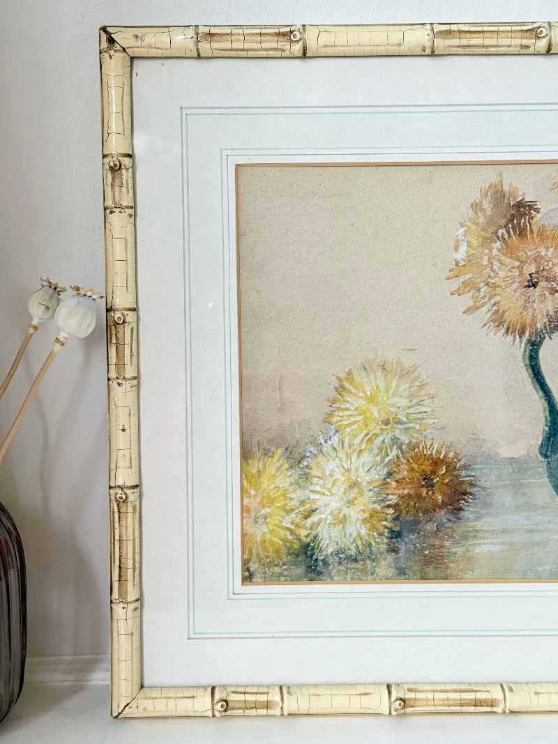 Vintage watercolour of chrysanthemums in green vase, under glass, in cream faux bamboo frame, photographed on white surface.
