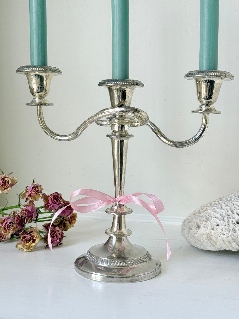 Vintage silver plated three arm candelabra with gadrooned detail and blue green taper candles styled on a white surface