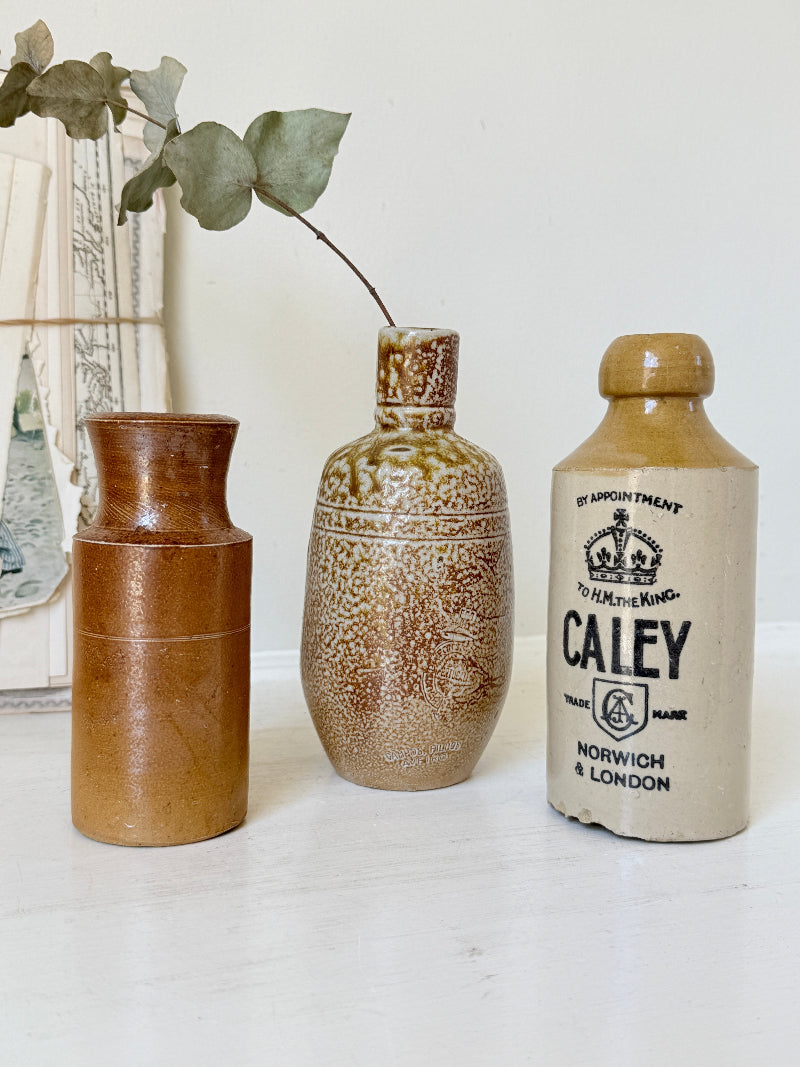 Three antique stoneware bottles, a printed Caley of Norwich and a Portuguese Campos Filhos, photographed on a white surface