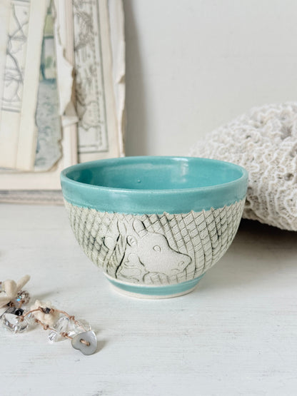 Hand thrown studio pottery bowl with turquoise glaze and hand decorated giraffe photographed on a white surface