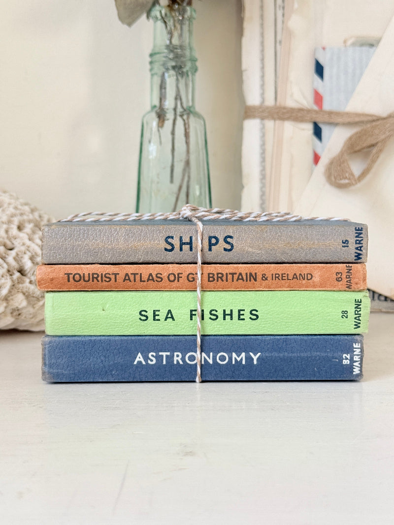 A stack of four vintage hardcover books tied together with twine, placed on a light surface. The spines read &