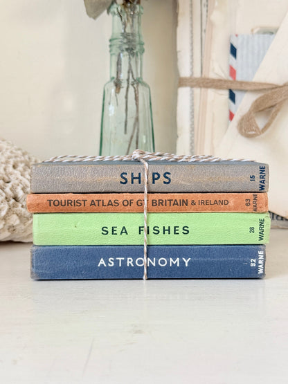 A stack of four vintage hardcover books tied together with twine, placed on a light surface. The spines read &