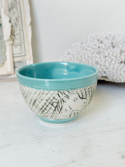 Hand thrown studio pottery bowl with turquoise glaze and hand decorated giraffe photographed on a white surface