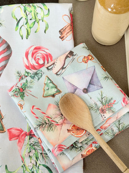Pair of pastel blue festive tea towels with candy cane and ribbon print, folded, photographed on a kitchen worktop
