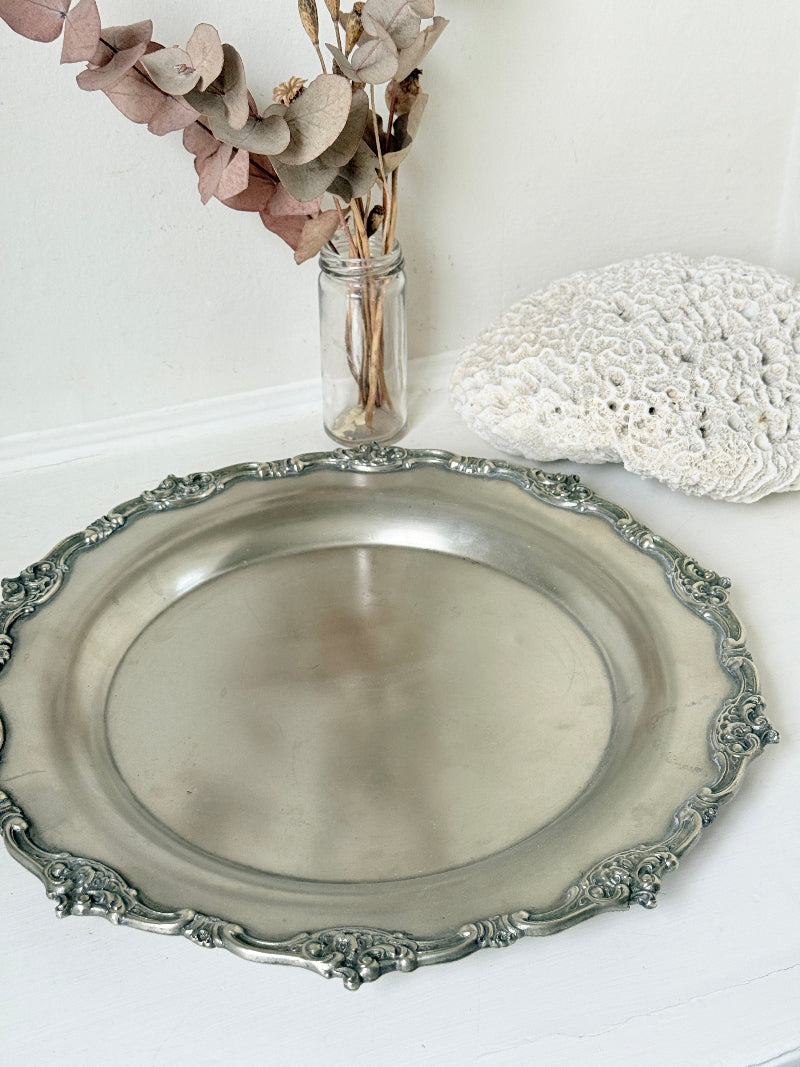 Vintage silvertone metal tray with ornate border, photographed on a white surface