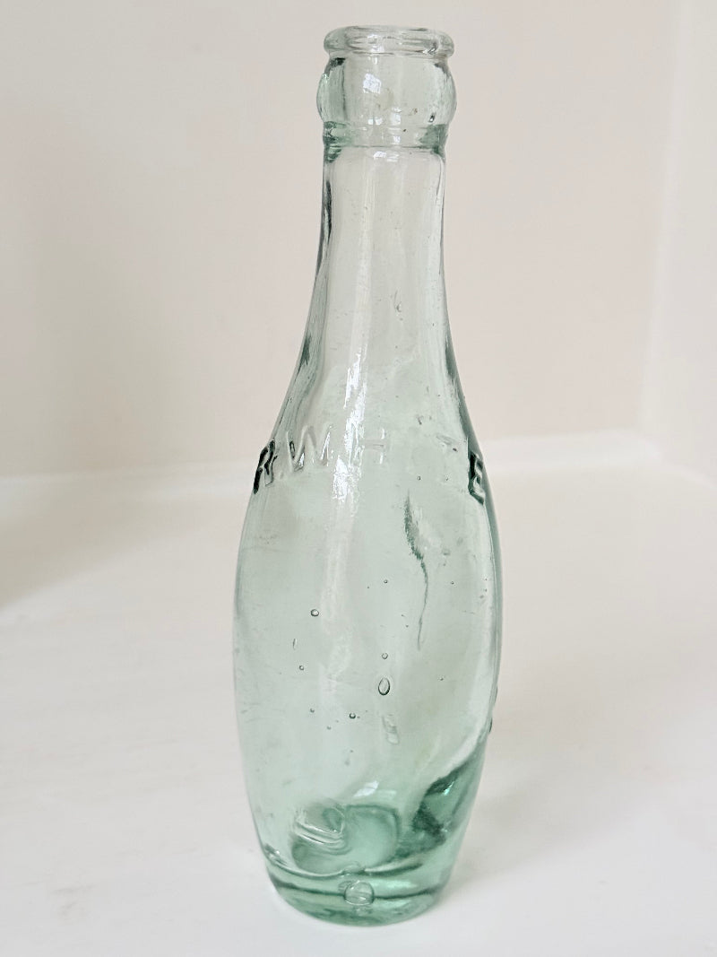 Trio of antique aqua glass bottles with embossed lettering, photographed on a white surface with dried stems
