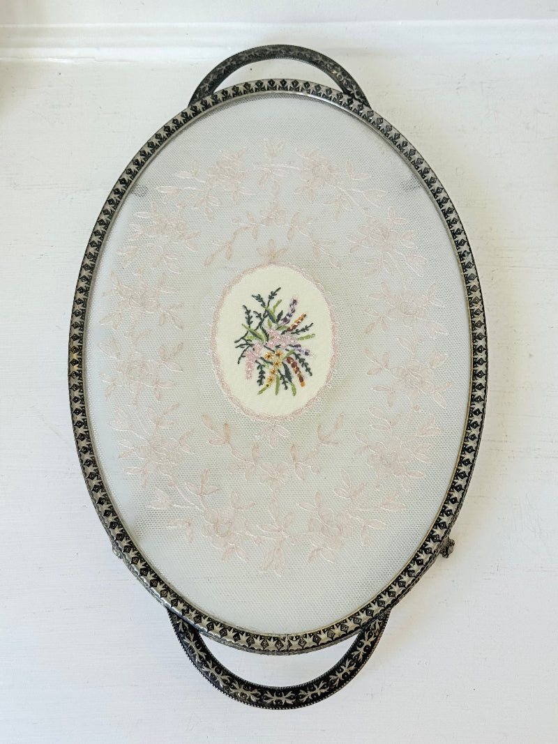Vintage oval metal tray with pierced gallery sides, twin handles, and floral centre, photographed on white surface.