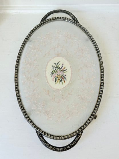 Vintage oval metal tray with pierced gallery sides, twin handles, and floral centre, photographed on white surface.