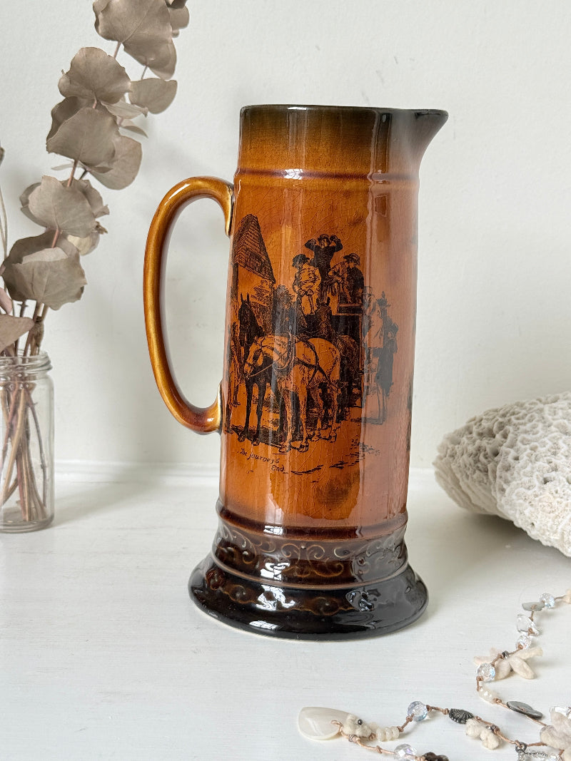 Antique Ridgways stoneware jug photographed on a white surface in amber treacle glaze with A Christmas Visitor black transfer scene and tall handle