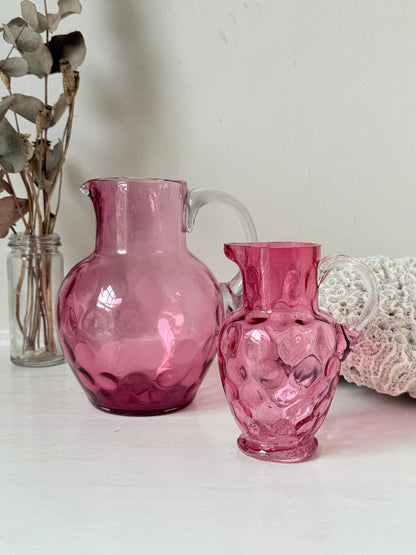 Vintage cranberry glass jugs, a pair with clear handles, photographed on a white surface