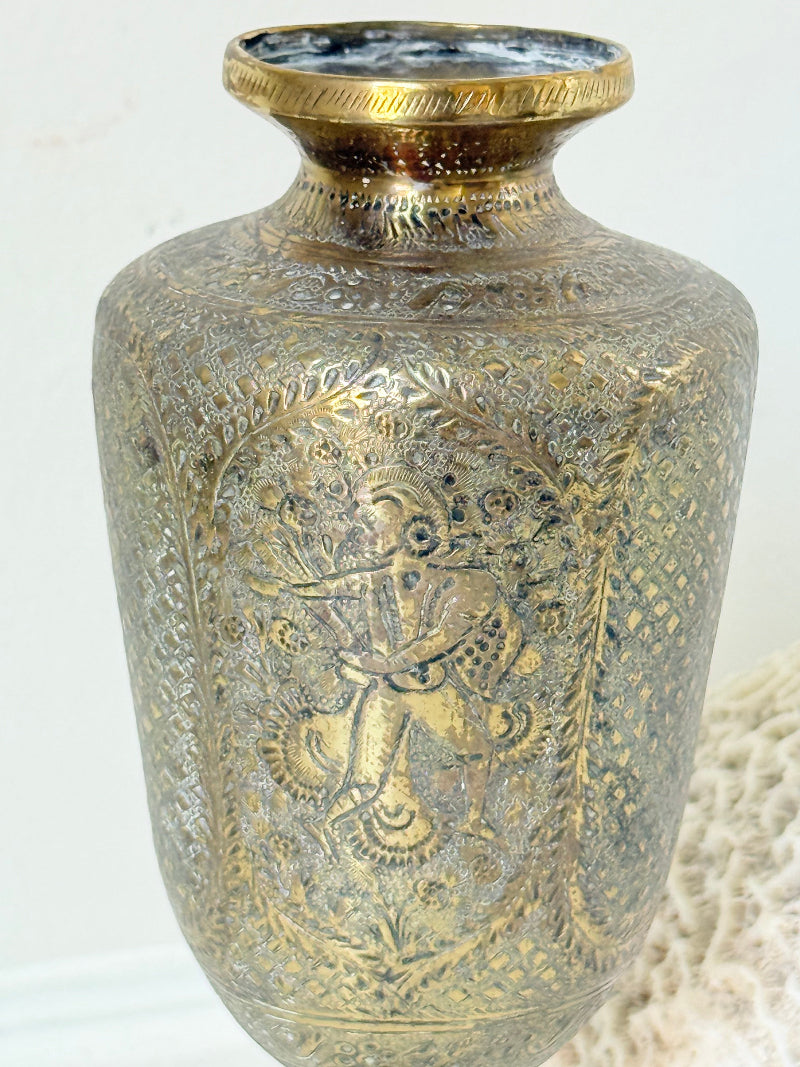Indian Benares brass chalice vase with figural panels and pedestal base, photographed on a white surface