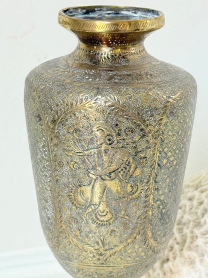 Indian Benares brass chalice vase with figural panels and pedestal base, photographed on a white surface