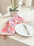 Warm peach coral and tropical fish print cotton tea towel with wooden forks on a marble surface beside cut glass
