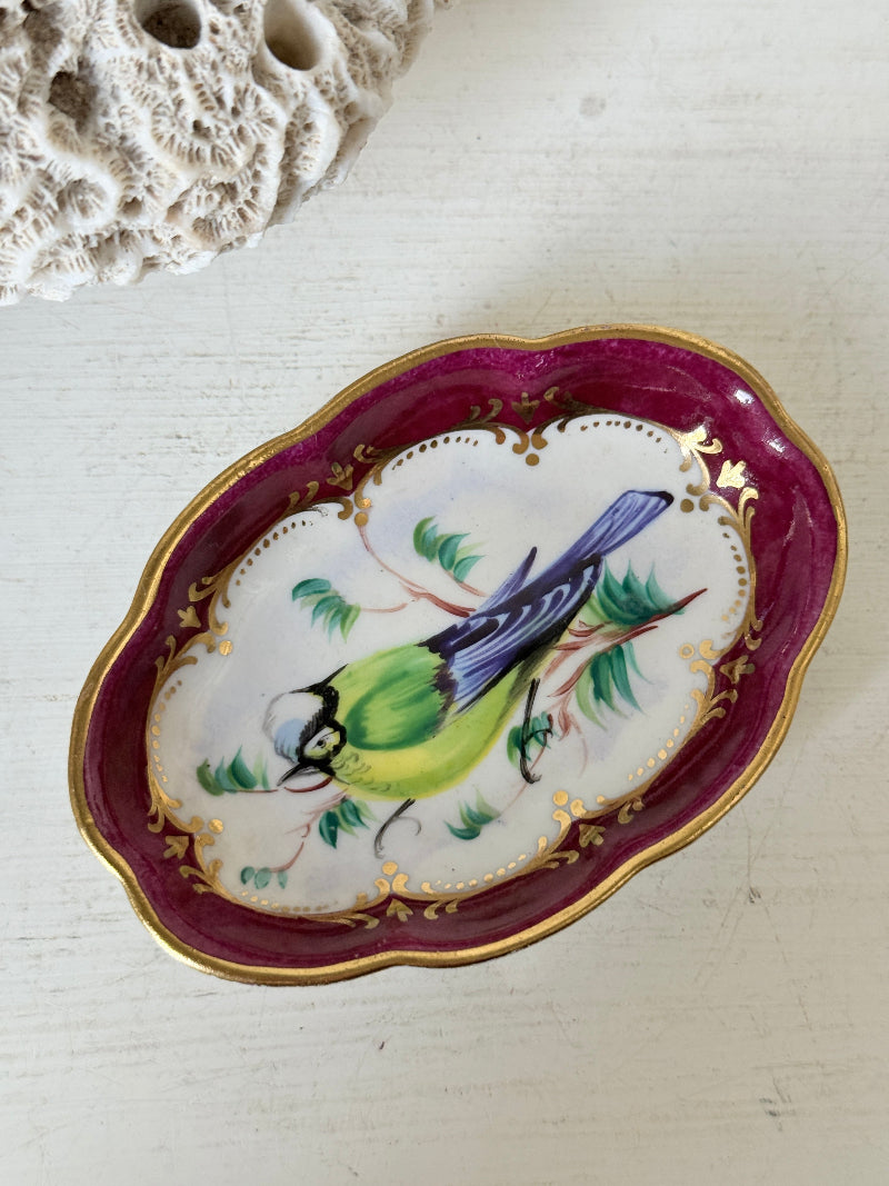 Vintage hand painted bird trinket dish with pink border and gilt detail photographed on a white surface