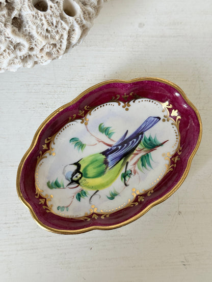 Vintage hand painted bird trinket dish with pink border and gilt detail photographed on a white surface