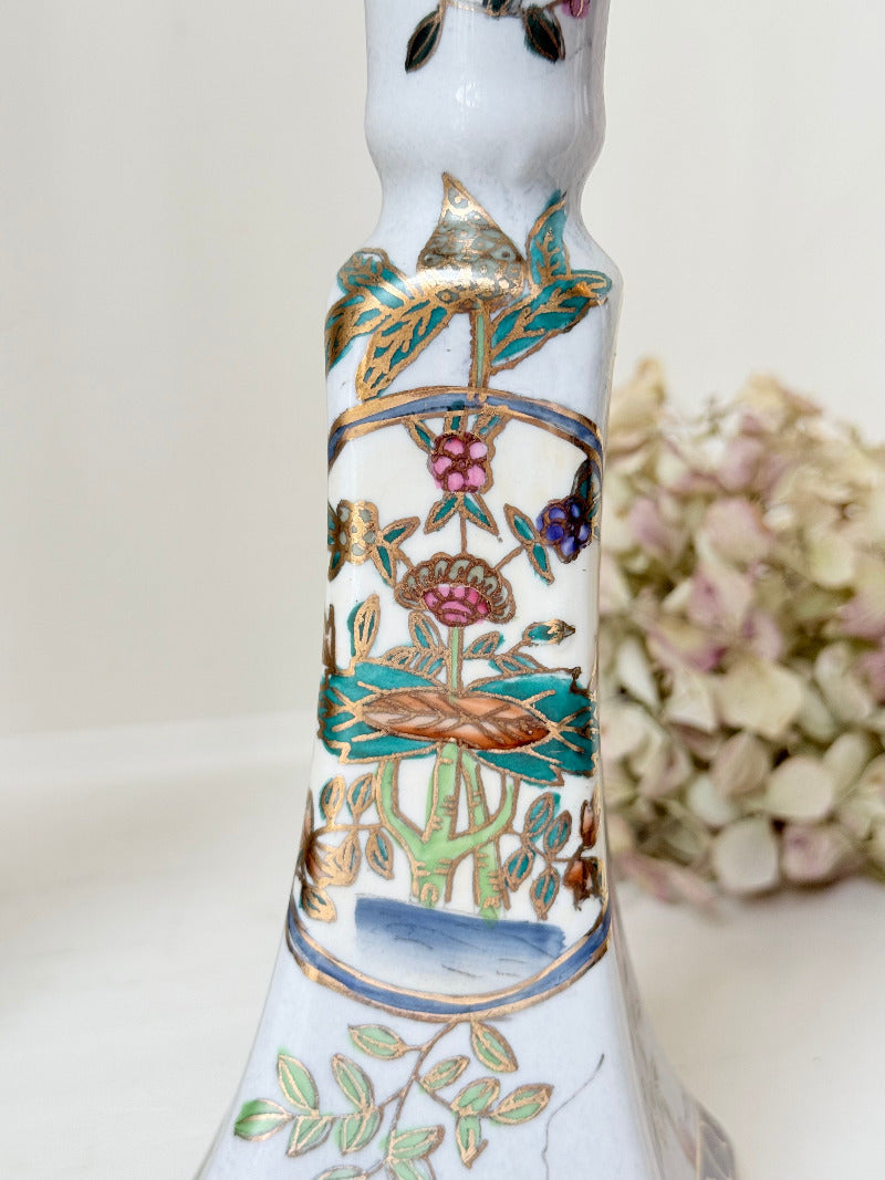 Pair of porcelain candle holders with hand-painted floral and vase motif in muted greens, pinks, and gold, styled with blush pink taper candles.