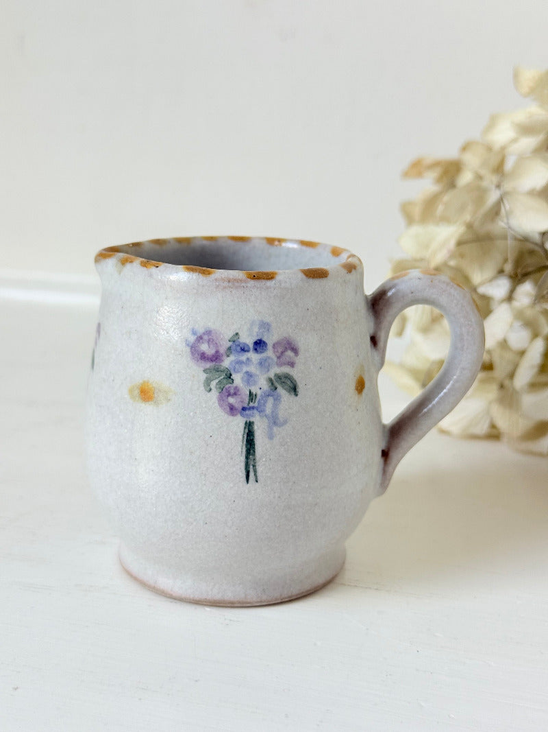 vintage studio pottery milk jug with hand painted lilac flowers and ochre rim photographed on white surface
