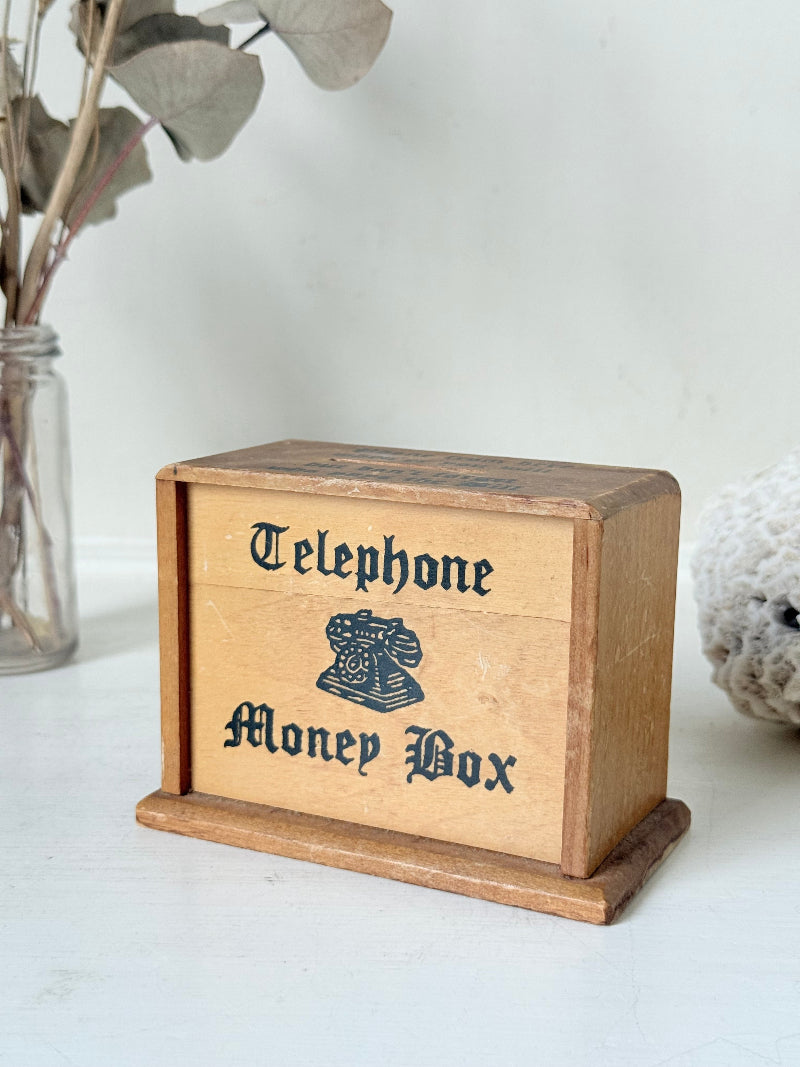 Vintage wooden telephone money box with printed lettering, photographed on a white surface