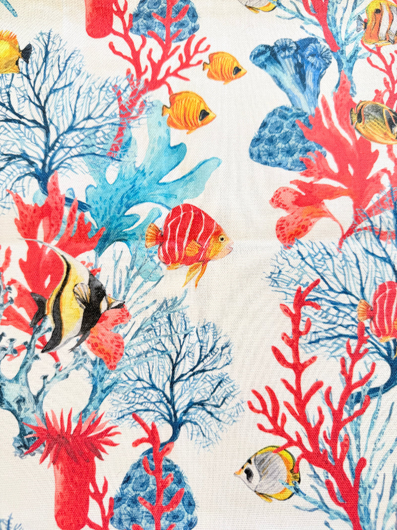 Coral reef print cotton tea towel in crisp white with colourful coral and tropical fish motifs, photographed indoors