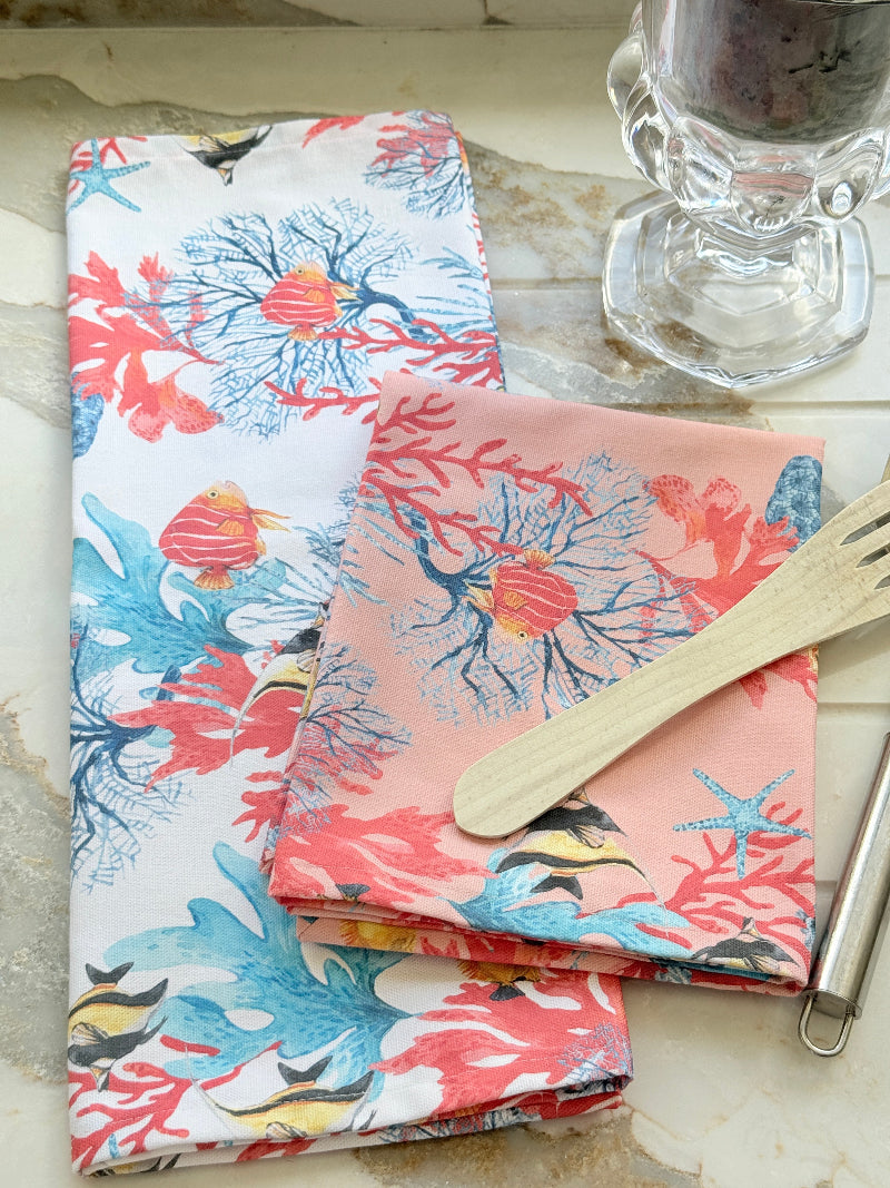 Warm peach coral and tropical fish print cotton tea towel with wooden forks on a marble surface beside cut glass