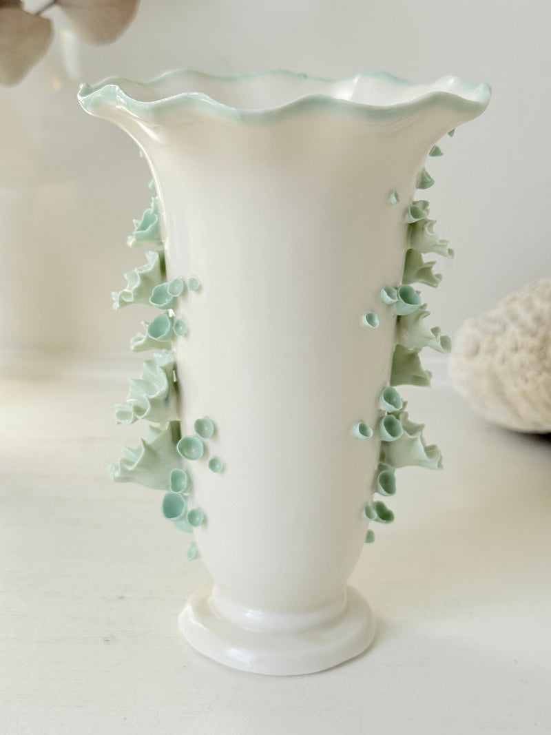 White Chessell Pottery studio vase with rippled rim and raised aqua floral decoration photographed on a white surface