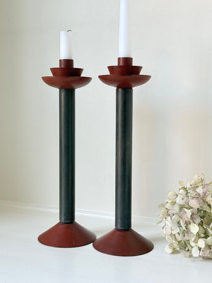 Pair of tall vintage metal candlesticks in black and burgundy, styled with white taper candles on a white surface.