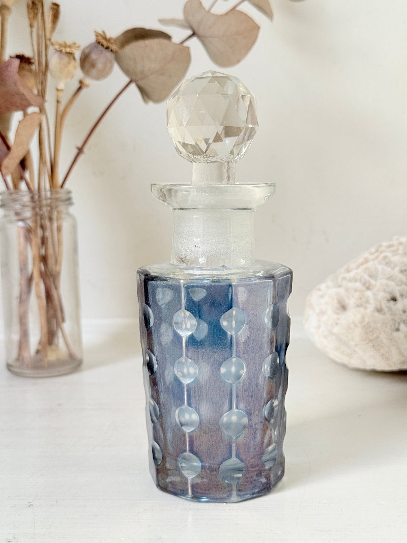Vintage decagon iridescent glass perfume bottle with raised dot pattern and clear faceted stopper, photographed on a white surface