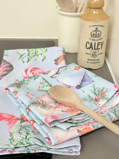 Pair of pastel blue festive tea towels with candy cane and ribbon print, folded, photographed on a kitchen worktop